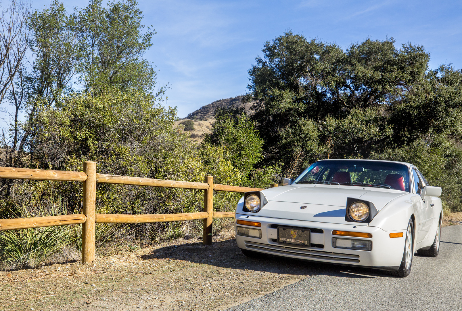 White Porsche 944 Turbo S in front of a fence with trees